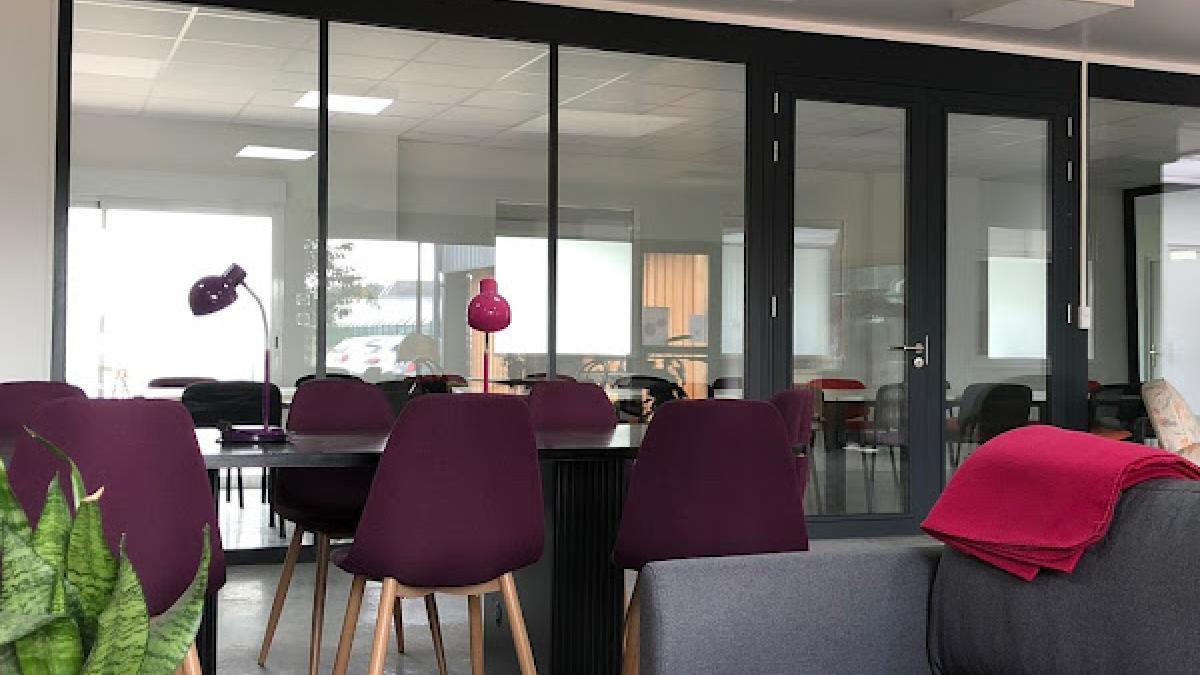 Aperçu de l'espace de coworking, avec ses espaces de détentes (canapé) une table de réunion, et une salle de réunion fermée et vitrée dans le fond